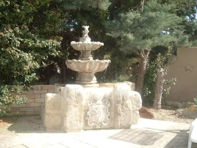 a stone fountain in a yard with trees at Gites Climatisés Piscine Chauffée La Balancelle in Saint-Rémy-de-Provence