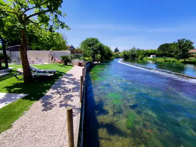 a river with blue water and trees on the side at Au Murmure de la Sorgue in LʼIsle-sur-la-Sorgue