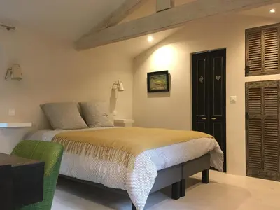 a bedroom with a bed and a green chair at La Calade, maison de village in Gordes
