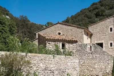 a stone building with a stone wall next to a mountain at La Ressence Luberon in Bonnieux