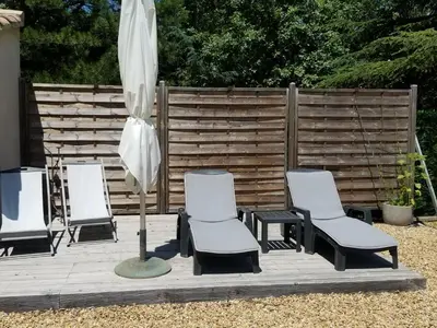three chairs and an umbrella on a wooden deck at La petite maison avec piscine face au Luberon in Robion en Luberon