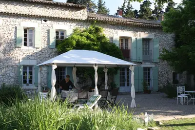 a man sitting under a white umbrella in front of a building at Le Mas d'Hermès in Plan-dʼOrgon