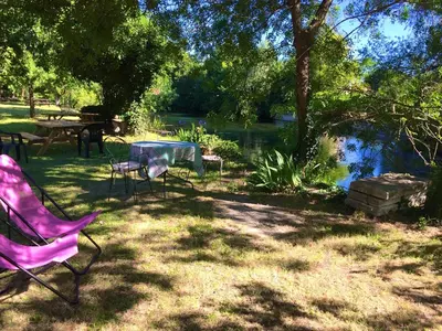 a picnic table and chairs in a yard with a pond at Mas Le Pont des Aubes in LʼIsle-sur-la-Sorgue