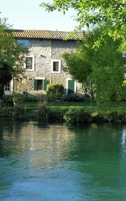 a building next to a river in front of a building at Mas Le Pont des Aubes in LʼIsle-sur-la-Sorgue
