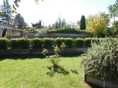 a garden with a retaining wall and some bushes at La maison bleue in LʼIsle-sur-la-Sorgue