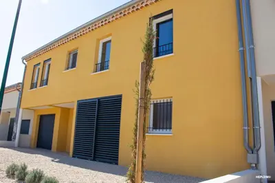 a yellow house with black garage doors and a tree at BASTIDE 7 in La Fare-les-Oliviers