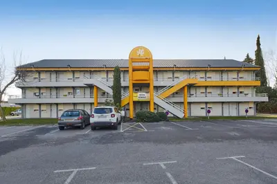 a large building with a large yellow structure in a parking lot at Premiere Classe Avignon Parc Des Expositions in Montfavet