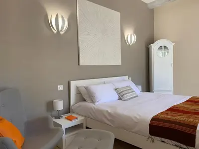 a white bedroom with a bed and a chair at MAS aux CEDRES in Lioux