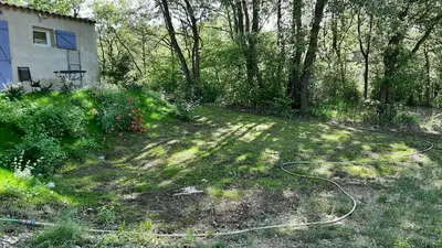 a yard with a hose in the grass next to a house at Le Cabanon in Sainte-Croix-à-Lauze