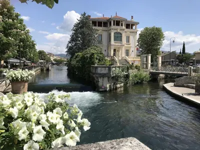 a view of a river with a building and flowers at La Magnanerie in LʼIsle-sur-la-Sorgue