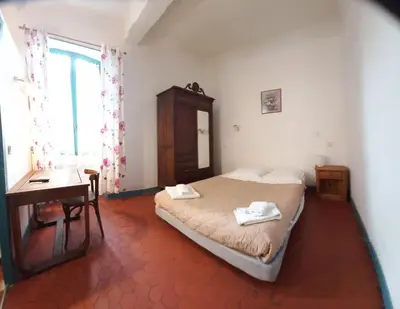 a bedroom with a bed and a desk and a window at Hôtel Du Cours in Pertuis