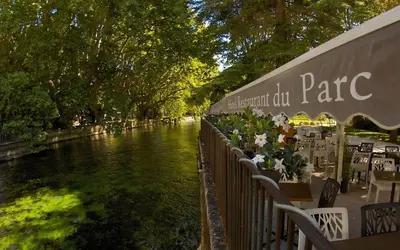 a river with tables and chairs next to a building at Logis Hôtel Restaurant du Parc in Fontaine-de-Vaucluse