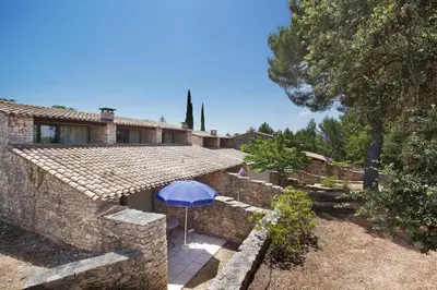 an external view of a stone house with a blue umbrella at Résidence Odalys La Bastide des Chênes in Gordes