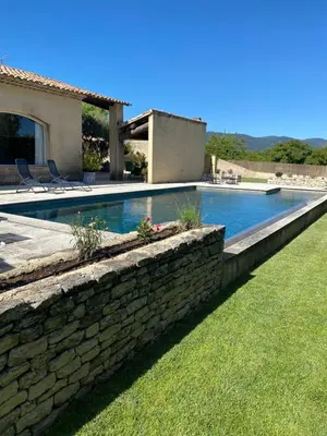 a swimming pool with a stone wall next to a house at Villa dans le LUBERON à 2 km de LOURMARIN in Lauris
