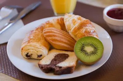 a white plate with croissants bread and a kiwi on it at Hôtel du Parc, Avignon Est, The Originals City, in Entraigues-sur-la-Sorgue