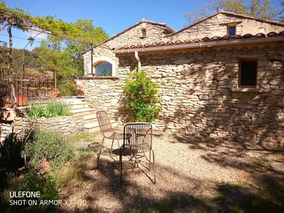 a stone house with two chairs in front of it at La maison jaune in La Roque-sur-Pernes