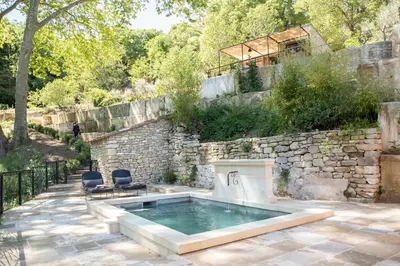 a pool with two chairs next to a stone wall at Les Cabanes de la Fontaine in Lacoste