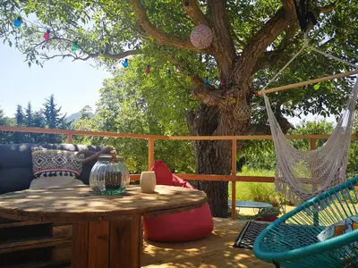 a patio with a table and chairs and a tree at Roulotte la clé du Luberon in Buoux