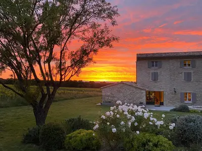 a sunset behind a building in a field with a tree at Le Cottage du Chat Blanc in Saint-Didier