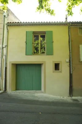 a building with a green garage door and a window at La Treille et L'Impasse in Ansouis