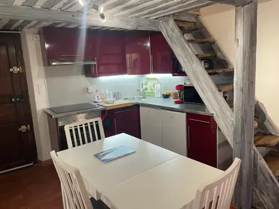 a kitchen with red cabinets and a white table with chairs at Studio cosy dans le centre-ville historique in LʼIsle-sur-la-Sorgue