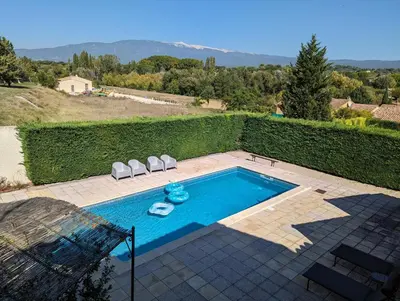 a swimming pool with two lawn chairs next to a hedge at Gîte Les Murmures du Ventoux in Mormoiron