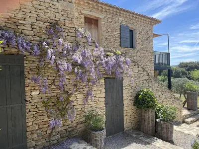 a stone building with purple flowers growing on it at Le Mas de Béthel in Gordes