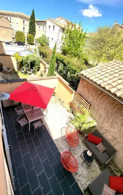 an outdoor patio with a red umbrella and chairs at Maison de village façon Loft, avec cour et airco, dans le centre historique in LʼIsle-sur-la-Sorgue