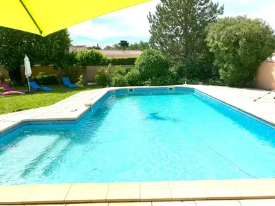 a large swimming pool with an umbrella in a yard at Villa et maisonnette provençales in Carpentras