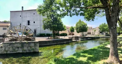 a river with a water wheel in front of a building at Quai du Félibre in LʼIsle-sur-la-Sorgue