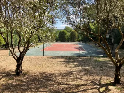 a tennis court with two trees in the foreground at Chambres dans le Luberon - Bois Romay in La Bastide-des-Jourdans