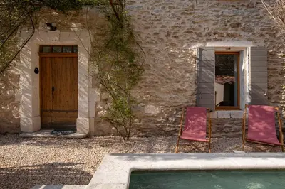 two chairs sitting in front of a building with a pool at Le Mas des Sablières in Oppède