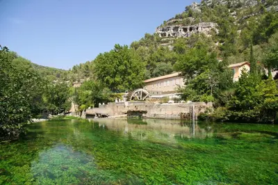 a river in front of a mountain with a building at Provence Now in Cabrières-dʼAvignon
