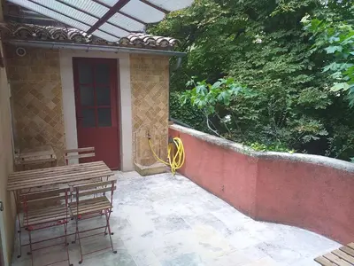 a patio with two benches and a red door at maison au coeur de Fontaine de Vaucluse, nichée sur le rocher et surplombant la sorgue in Fontaine-de-Vaucluse