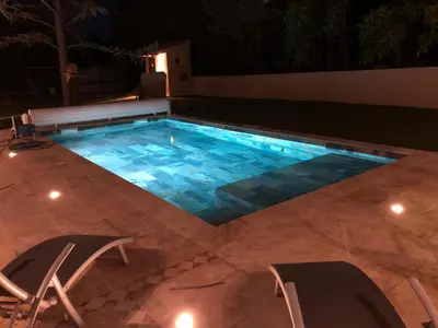 a swimming pool at night with chairs and a bench at Au milieu des Piboules de Provence. in LʼIsle-sur-la-Sorgue