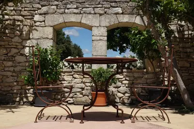 a table and two chairs in front of a stone wall at Les Néfliers Gîte in Céreste