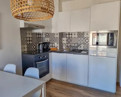 a kitchen with white cabinets and a table and a chandelier at Un balcon sur les toits d'Aix in Aix-en-Provence