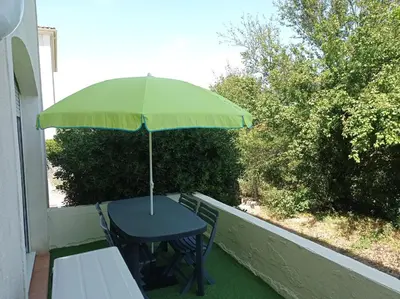 a table with a green umbrella on a balcony at LE SOLEIL DU LUBERON - T2 avec Terrasse, Parking et Clim in LʼIsle-sur-la-Sorgue