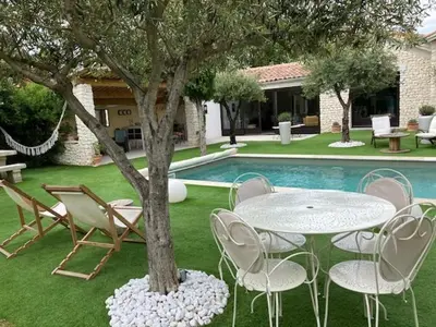 a table and chairs around a tree next to a pool at La Maison 1440 in LʼIsle-sur-la-Sorgue