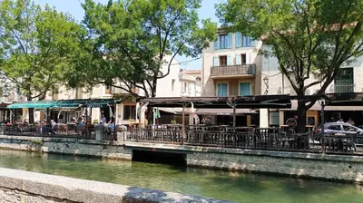 a group of people sitting at tables by a river at Vue imprenable sur la Sorgue in LʼIsle-sur-la-Sorgue