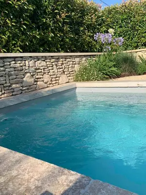 a swimming pool with a stone wall and blue water at Le Cabanon de Livia avec piscine privée in Cucuron